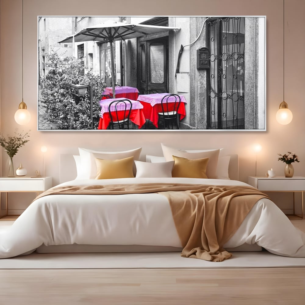 Tablou canvas cu cafenea stradala vintage alb negru cu pete de rosu, in rama de aluminiu argintiu, pe perete intr-un dormitor